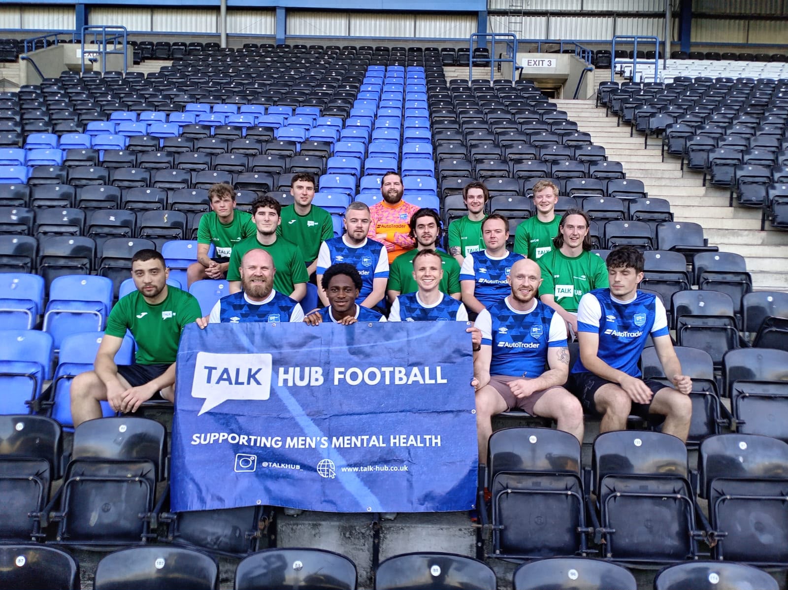 TalkHub football players in green and blue kits sitting in stadium stands holding a Talk Hub Football banner