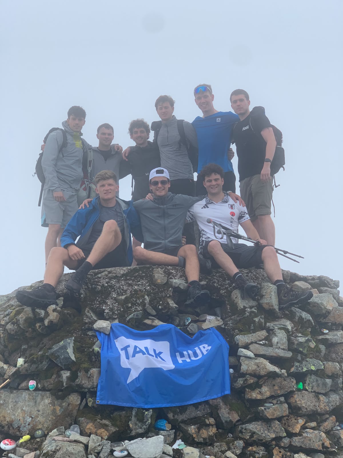 Group of fundraisers on a misty mountain summit cairn with a TalkHub flag