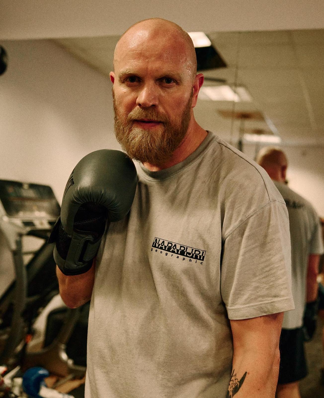 Phil in a grey T-shirt holding up a boxing glove in the gym
