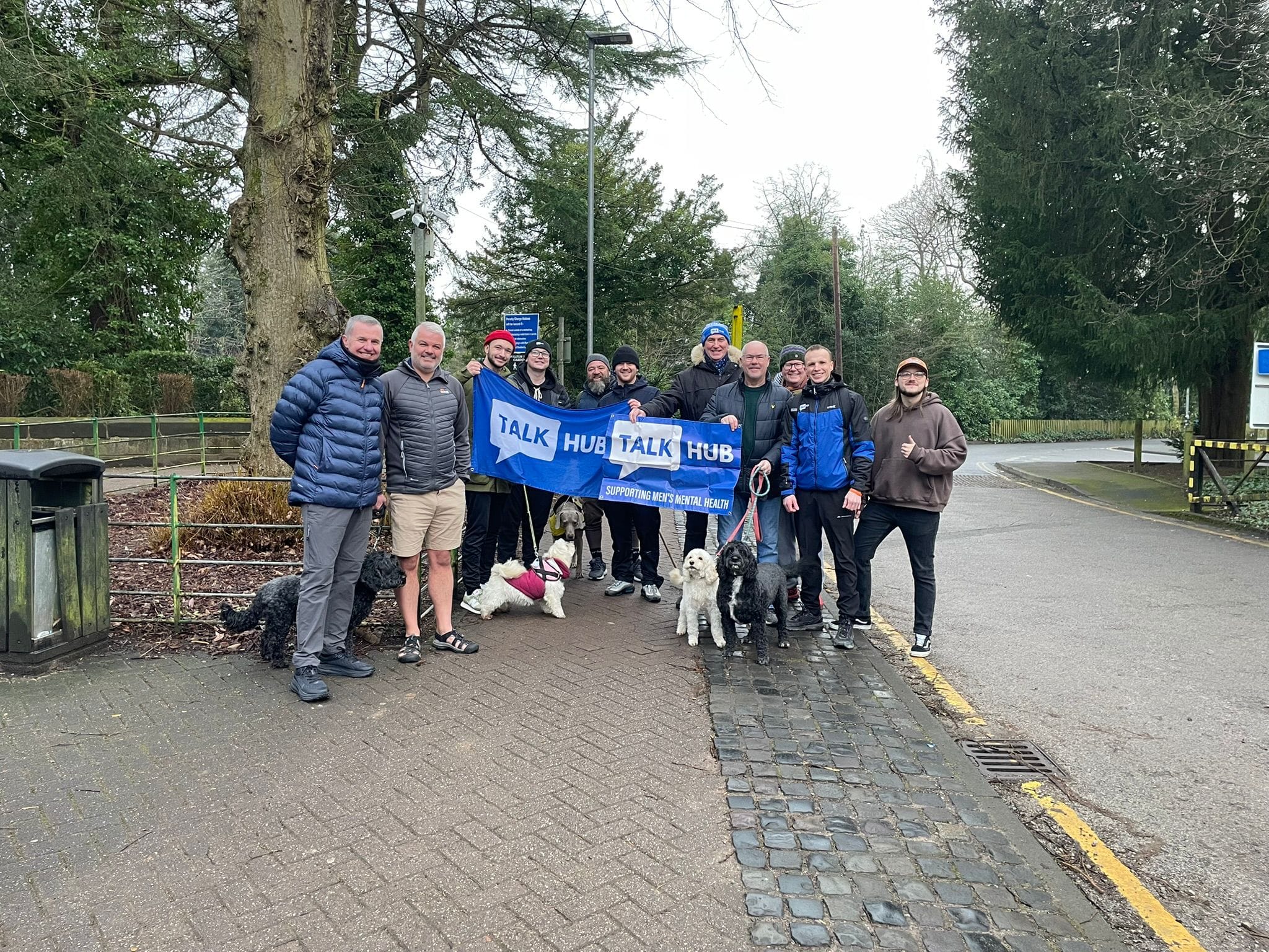 A group of TalkHub men and their dogs on a tree-lined path holding TalkHub banners
